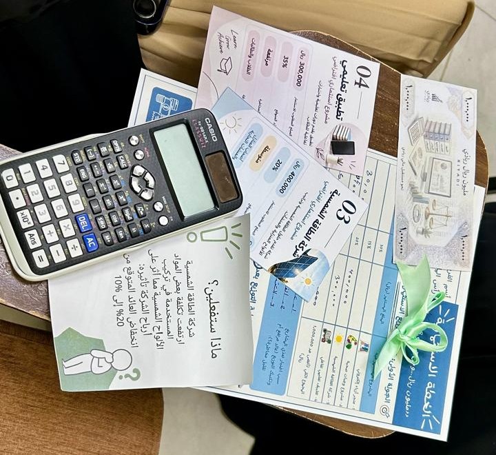 آلة حاسبة ونشرات تعريفية وأوراق عمل عن الادخار والميزانية الشخصية معروضة ضمن فعالية توعوية بالكلية